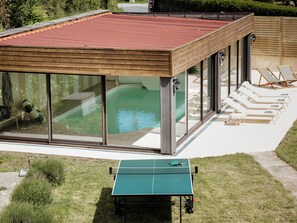 Une maison moderne dotée d’une piscine, de chaises longues et d’une table de ping-pong.