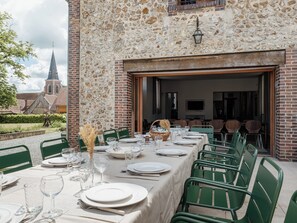 Un espace de restauration en plein air avec un mur en pierre, des chaises vertes et une table dressée pour un repas.