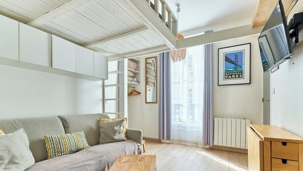 A modern living room with a sofa, a wooden table, and a TV mounted on the wall. - Opera · 9th · Cosy Studio with Mezzanine – managed by Mey Agency (Paris)