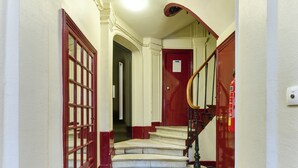 A staircase with a red door at the top, a fire extinguisher on the wall, and a light fixture above. - Opera · 9th · Cosy Studio with Mezzanine – managed by Mey Agency (Paris)