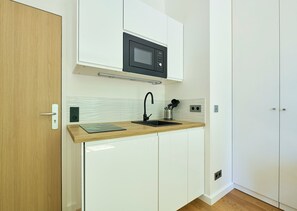 A compact kitchen with a microwave, sink, and wooden countertop. - Auteuil · 16th · Bright & Minimalist Studio – managed by Mey Agency (Paris)