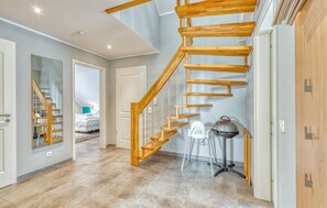 Ein modernes Interieur mit einer Holztreppe, einem Bett im Hintergrund und einem Stuhl neben einem Tisch.