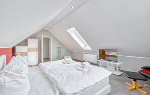 Ein modernes Schlafzimmer mit schrägverdeckter Decke, einem Oberlicht, einem Bett, einem Fernseher und einem Schreibtisch.