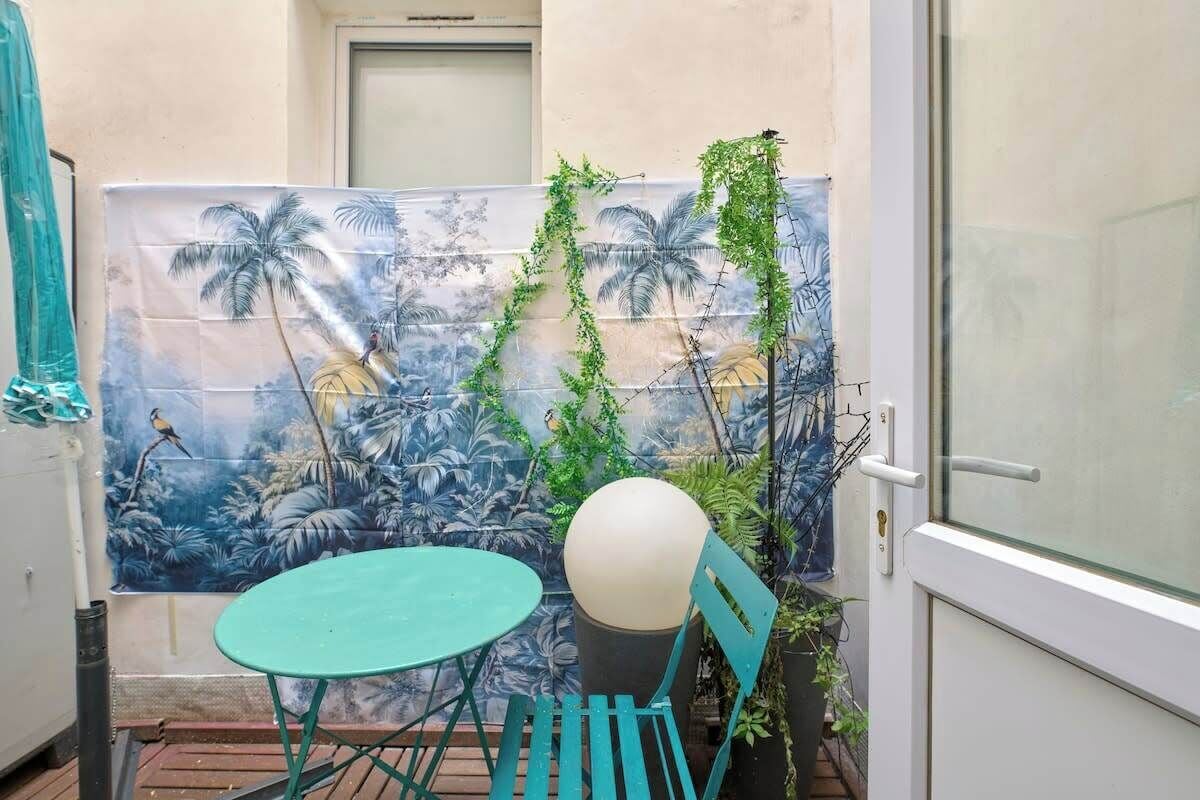 A small outdoor seating area with a table and chairs, a decorative wall with a tropical mural, and a door with a glass panel.