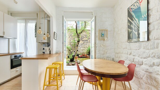 Una cocina moderna con una isla central, un área de comedor con una mesa redonda y sillas rojas, y una pared de ladrillo blanco con un cuadro enmarcado.