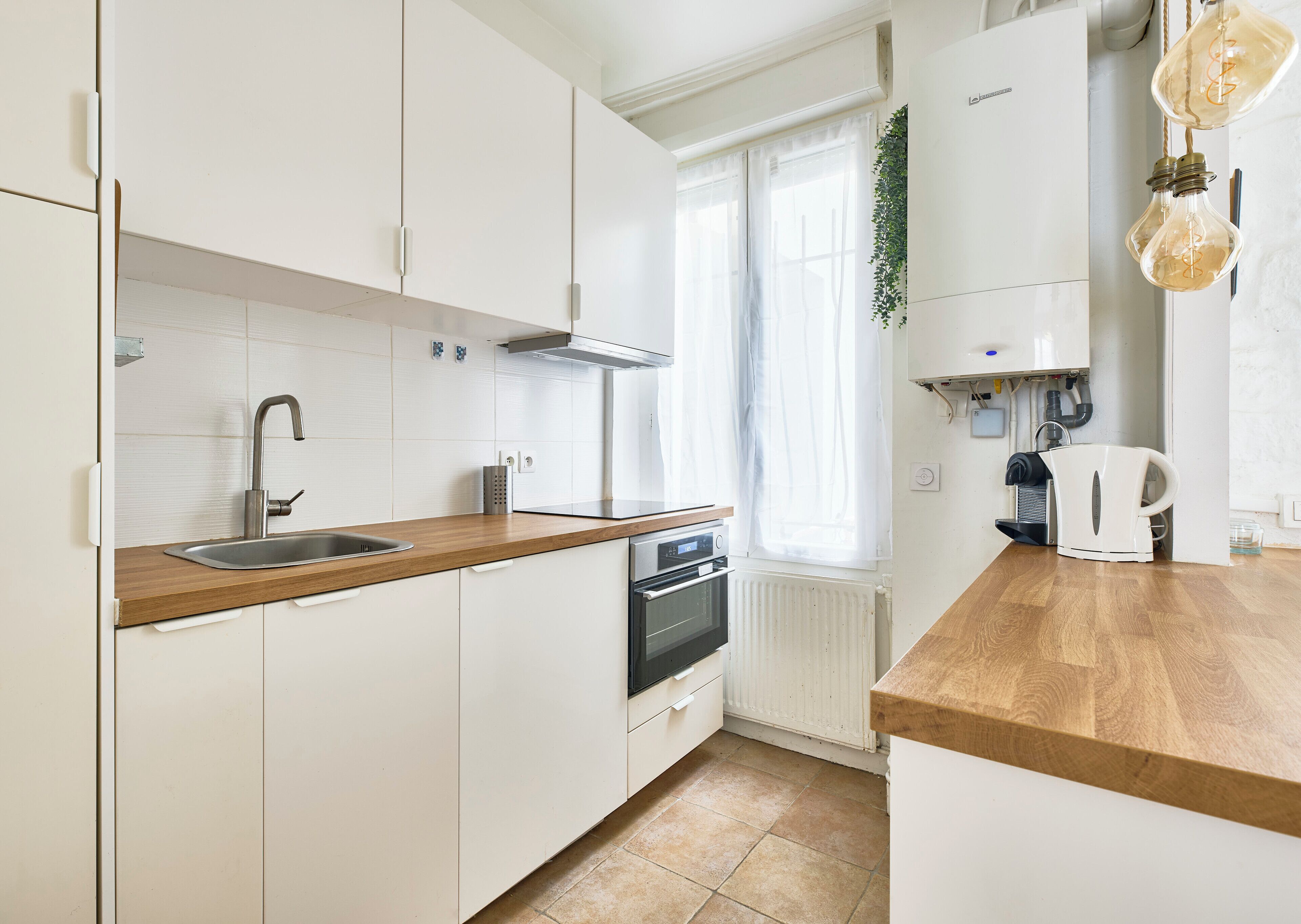 A modern kitchen with white cabinets, a stainless steel sink, a built-in oven, and a coffee maker.