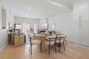 Ein modernes Wohnzimmer mit einem runden Holzes Esstisch, sechs Stühlen, einer Couch, einem Fernseher und einem Kamin.