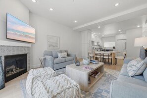 Ein modernes Wohnzimmer mit Kamin, Flachbildfernseher, Sofa, Couchtisch und Essbereich mit Stühlen und Tisch.