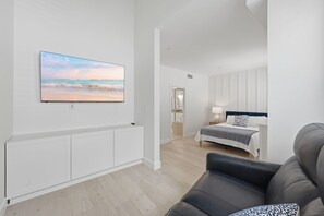 Ein modernes Wohnzimmer mit Flachbildfernseher, einer Couch, einem Bett und Blick auf den Strand.