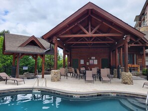 A covered outdoor area with a pool, lounge chairs, and a wooden pavilion. - Cozy 2-bedroom condo with mountain views, amazing sunsets, pool, hot tub, & more (Pigeon Forge)