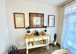 Une pièce avec une console en bois, deux plantes en pot, un miroir et une fenêtre donnant sur un paysage.