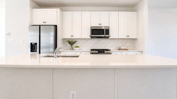 Una cocina moderna con armarios blancos, un refrigerador de acero inoxidable, un microondas y una estufa a gas.