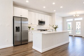 Una cocina moderna con armarios blancos, un refrigerador de acero inoxidable, un microondas y una isla central con un lavamanos.