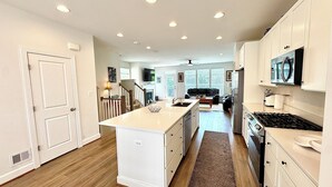 Una cocina moderna con muebles blancos, una isla central y un área de comedor con sofá.