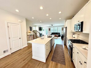 A modern kitchen with white cabinetry, a central island, and a dining area with a sofa. - Spectacular 4 bed/3.5 Bath Chantilly/Northern Virginia Townhouse (Chantilly)