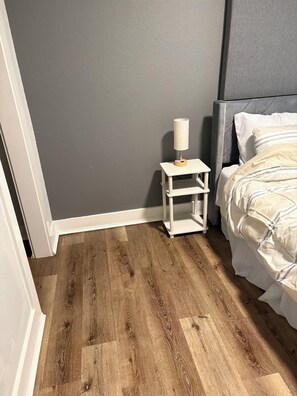 Una camera da letto con un letto, un comodino, una lampada e una parete grigia.