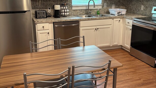 A modern kitchen with white cabinets, stainless steel appliances, a granite countertop, and a dining area with a wooden table and metal chairs. - Tranquil 1-bedroom apartment with AC in cozy Alvin (Alvin)