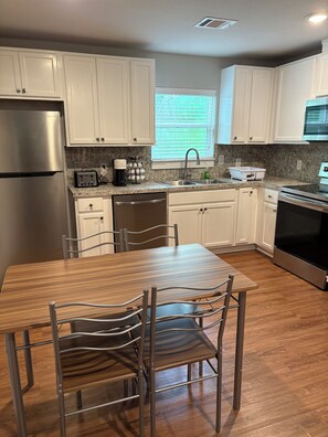 Eine moderne Küche mit weißen Schränken, Edelstahlgeräten, einer Arbeitsplatte aus Granit und einem Essbereich mit einem Holztisch und Metallstühlen.