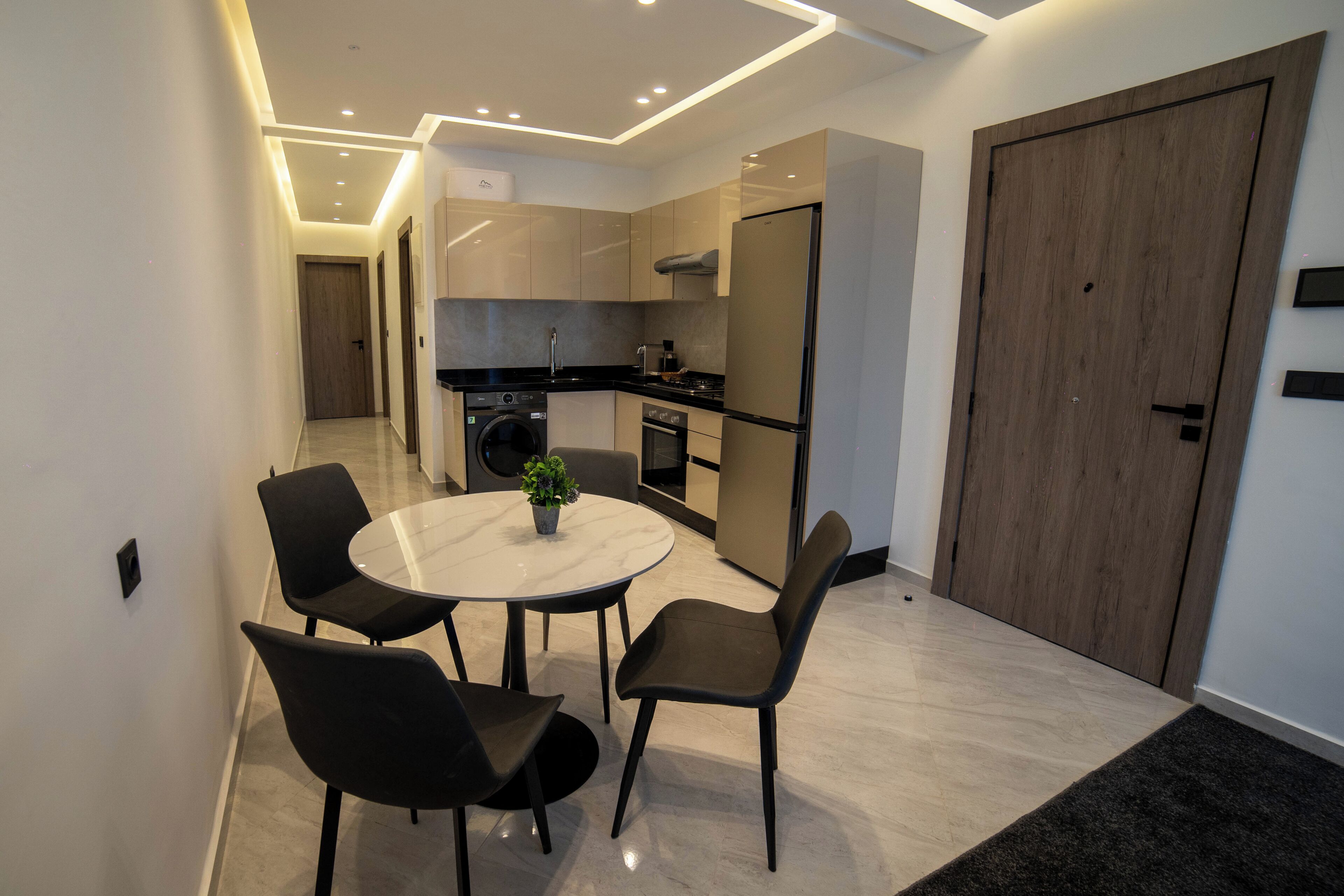 Une cuisine moderne avec un coin repas, comprenant une table ronde et des chaises, un lave-linge et une grande porte en bois.