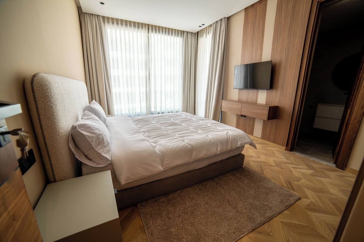 Una habitación de hotel moderna con una cama grande, un televisor de pantalla plana y suelo de madera.