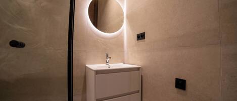 Une salle de bain moderne avec un miroir rond, un lavabo blanc et un luminaire fixé au mur.