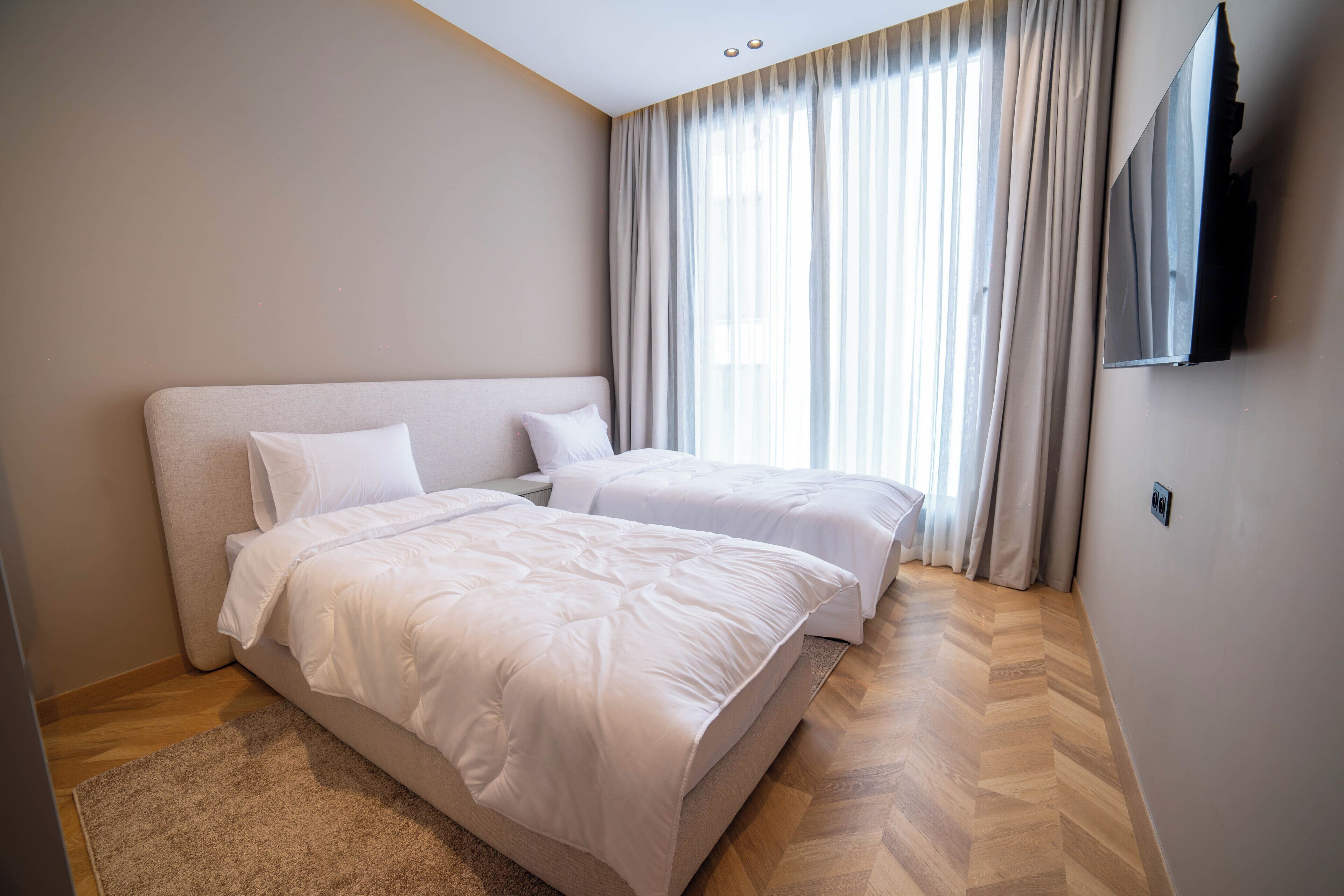 A bedroom with two beds, a TV, and a large window with curtains.