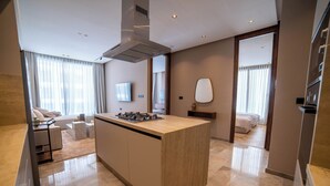 Una cocina moderna con una isla central, un área de comedor con sofá, y un dormitorio visible a través de una puerta abierta.