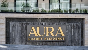 Letrero que indica 'AURA Luxury Residence', con fachada de madera y un edificio moderno al fondo.