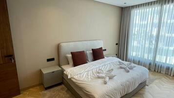 Ein Hotelzimmer mit einem großen Bett, einem Nachttisch, einem Schrank aus Holz und Blick ins Freie durch das Fenster.