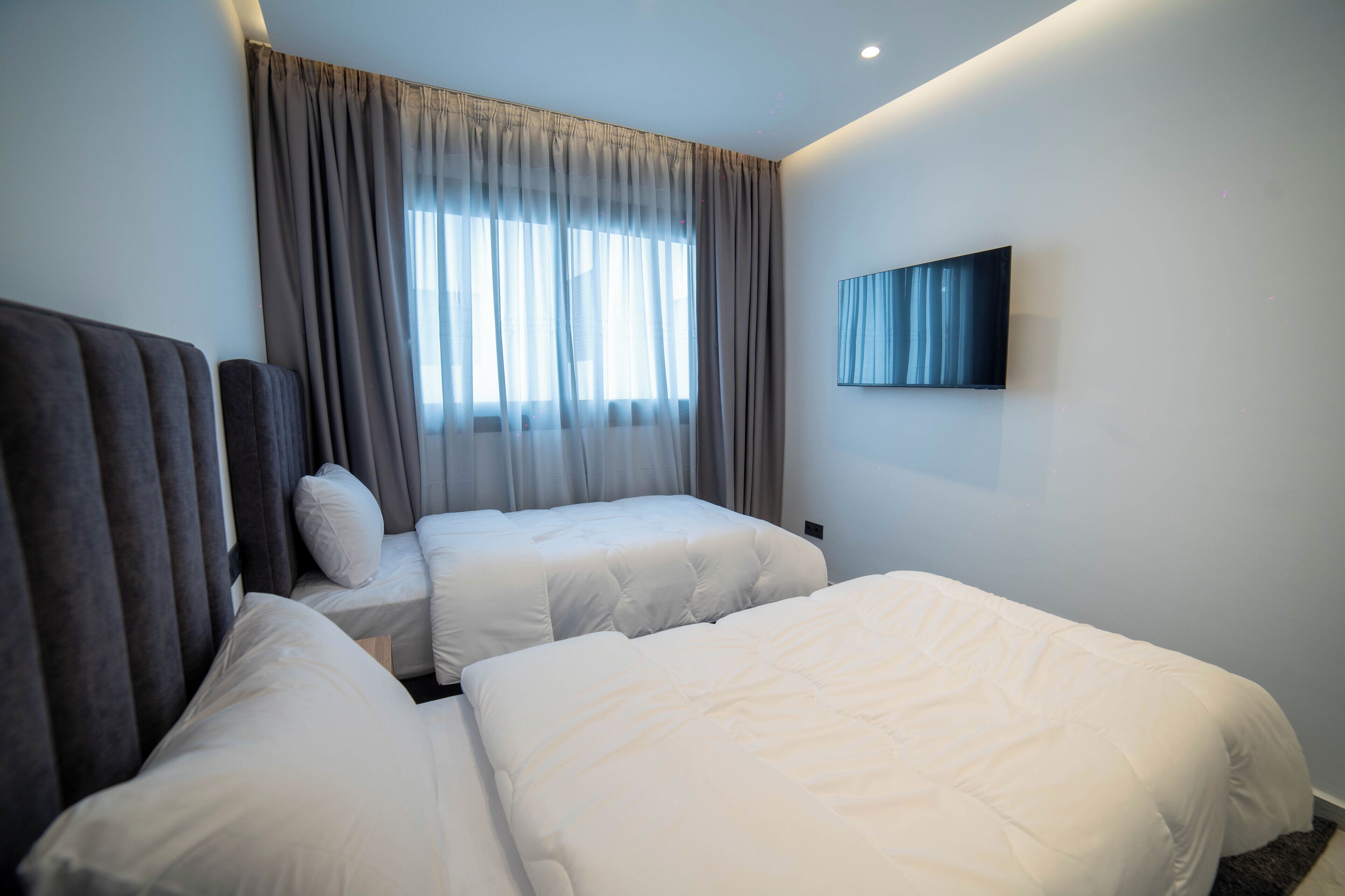 Habitación de hotel con dos camas, un ventanal con cortinas, un televisor de pantalla plana montado en la pared y un diseño moderno.