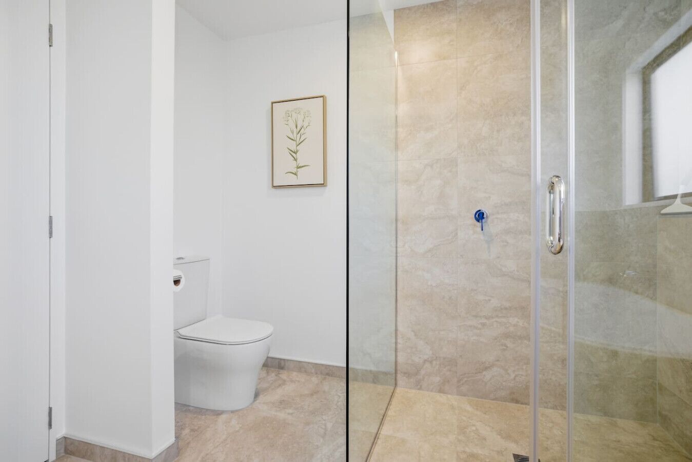 Un baño con inodoro, cabina de ducha de vidrio e imagen en el marco en la pared.