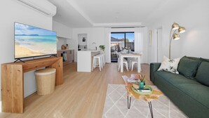 Ett modernt vardagsrum med en TV, en grön soffa, en matplats och ett kök.