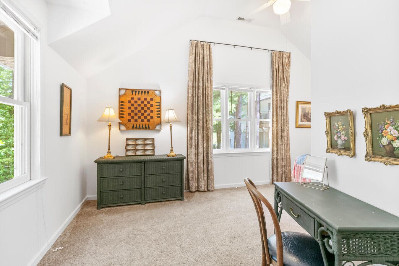 A room with a green dresser, two lamps, a chessboard, a window with curtains, and framed pictures on the wall.