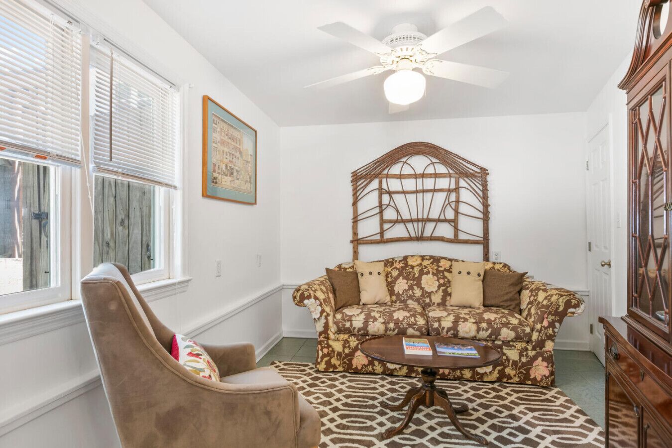 A room with a sofa, a chair, a table, a ceiling fan, and a picture on the wall.