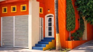 Um edifício com fachada laranja vibrante, uma palmeira e um conjunto de degraus que levam a uma porta.