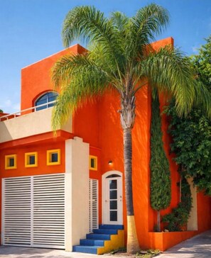 Un bâtiment à la façade d’un orange vif, avec un palmier et un escalier menant à une porte.