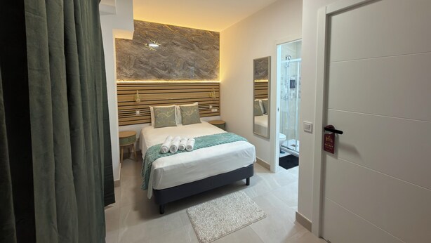 Una habitación de hotel moderna con cama, mesita de noche, espejo, zona de ducha y equipo de aire acondicionado.