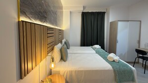 Una habitación de hotel con una cama grande, cabecera de madera, lámpara de noche, manta verde y un armario.
