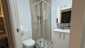 Un baño moderno con ducha de vidrio, inodoro y lavamanos con espejo.
