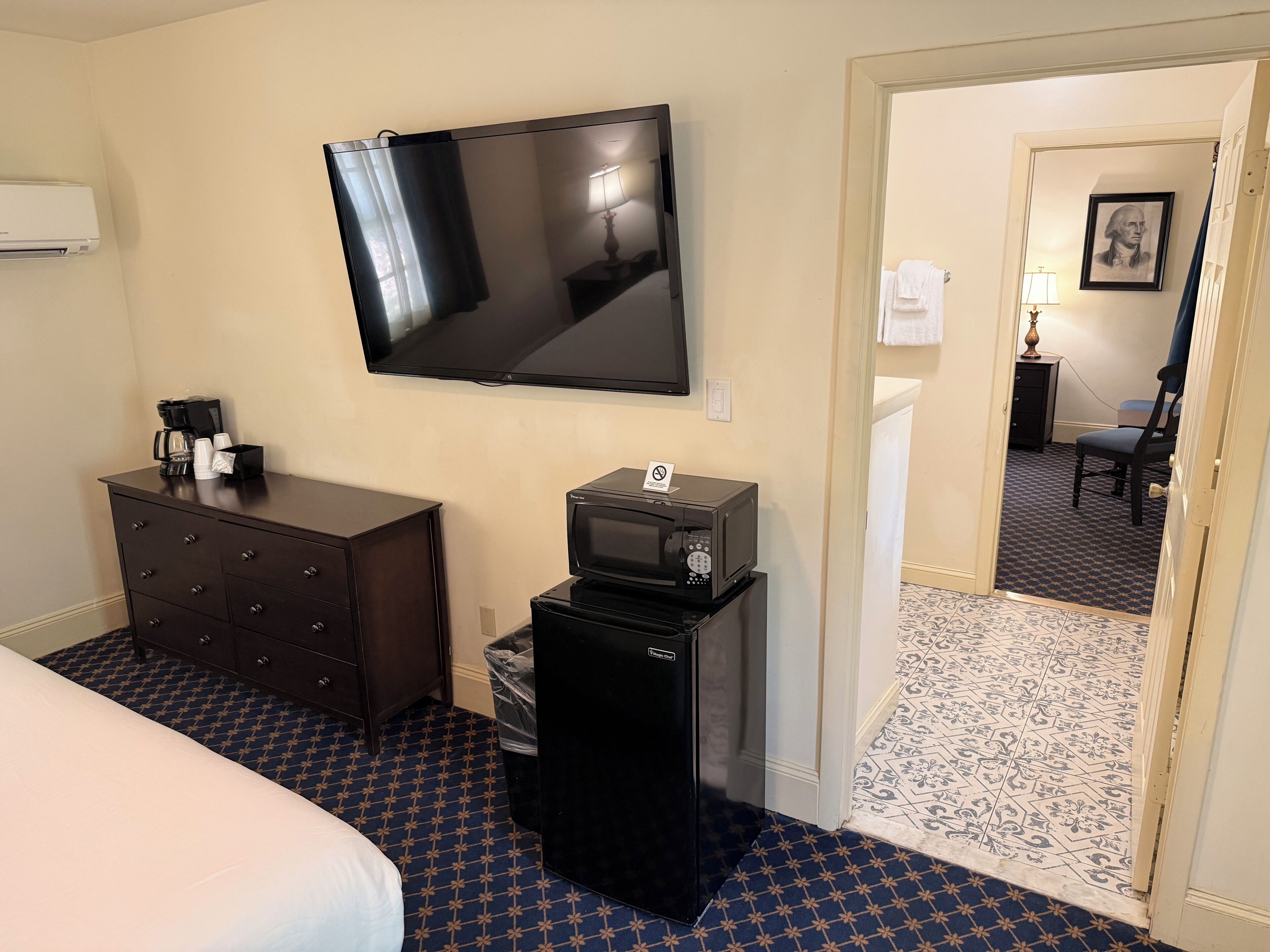 Una habitación de hotel con cama, cómoda, televisión, microondas y contenedor de basura.