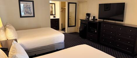A hotel room with two beds, a TV, a dresser, and a ceiling fan.