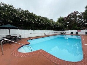 A rectangular swimming pool with a brick border, surrounded by a white fence and green chairs. - Princess Anne Hotel, SureStay Collection by Best Western (Williamsburg)