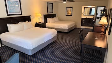 A hotel room with two beds, a desk, a chair, a lamp, and a ceiling fan.