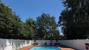 A rectangular swimming pool with a brick border, surrounded by a white fence, and trees in the background. - Princess Anne Hotel, SureStay Collection by Best Western (Williamsburg)