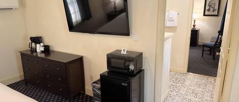 A hotel room with a flat-screen TV, a dresser, a microwave, and a bed.
