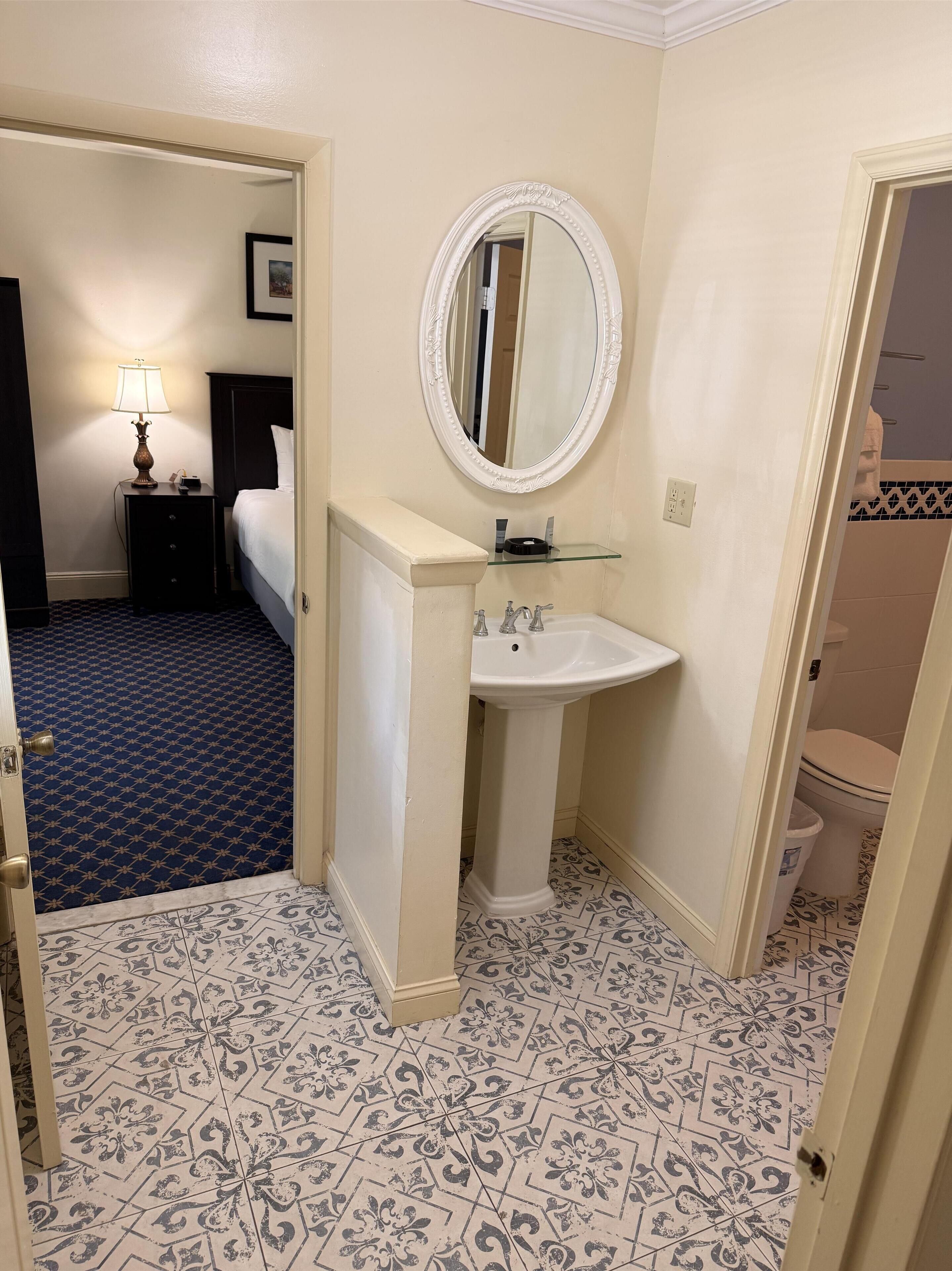 Un bagno d'hotel con un lavabo su piedistallo, uno specchio rotondo e un pavimento decorato.