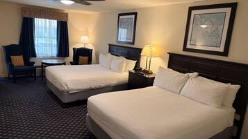 Habitación de hotel con dos camas, un escritorio, una silla, un ventilador de techo y una ventana con cortinas.