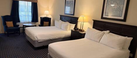 A hotel room with two beds, a desk, a chair, a ceiling fan, and a window with curtains.