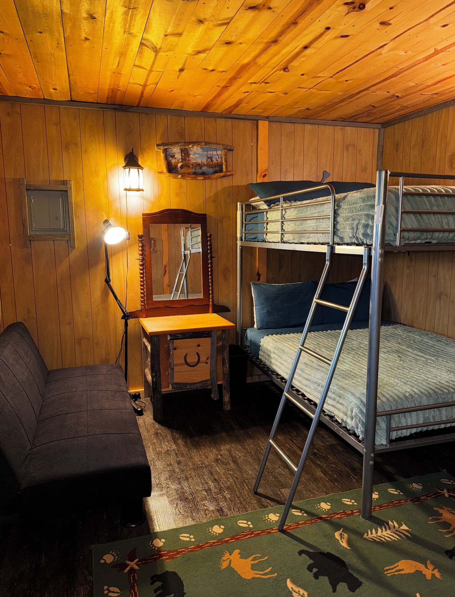 A wooden cabin room with bunk beds, a desk, a chair, a mirror, and a lamp.