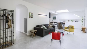 Ein modernes Wohnzimmer mit einer Couch, einem roten Sessel, einem Essbereich und einer Küche im Hintergrund.
